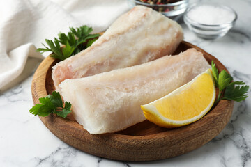 Fresh raw cod fillets with parsley and lemon on white marble table, closeup