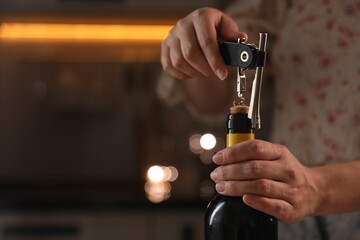 Woman opening wine bottle with corkscrew on blurred background, closeup. Space for text