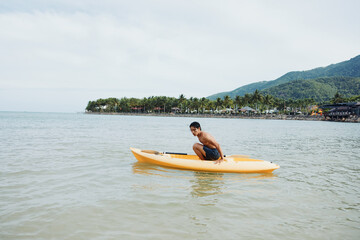 Happy Asian man enjoying kayaking in azure tropical waters with palm-fringed beach as backdrop.