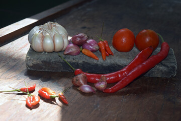 Cayenne pepper, large red chilies, shallots and garlic are on a wooden table with wooden dishes...