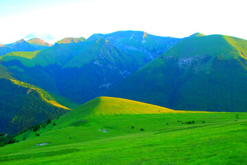 Powerful scenery in Piani di Ragnolo with almost uniform pastures on a slope in the foreground and the spectacular, energizing display of Sibillini mountains in the background, under uniform sky