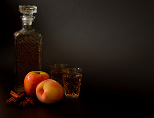 Apple-peach liqueur with cinnamon and anise on a black background, homemade alcohol in a decanter and glasses with spices and ripe fruits.