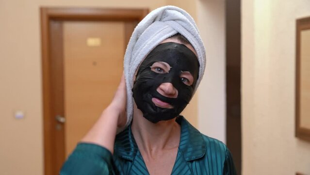 Woman with black mask on her face, head wrapped in towel, compulsively harasses, ridiculously flirts with hotel neighbor Lonely old maid with cream on face, flirting while straightening hair with hand