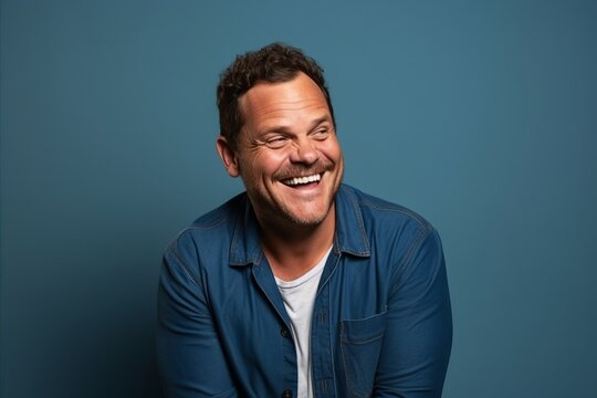 Portrait of a happy mature man laughing against blue studio background.