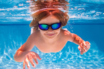 Summer child boy relax at aquapark. Summertime vacation. Little kid swim underwater in pool. Kid wearing summer goggles swims under water in poolside. Underwater photo.