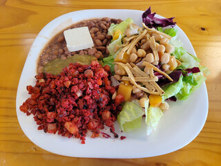 A vibrant plate featuring spicy soy chorizo, pinto beans with green salsa, a cube of cheese, and a...