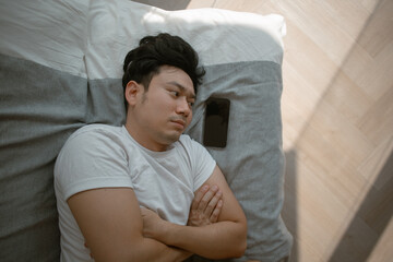 Social media depression. Sad and depressed asian man lie on the sofa with mobile phone.