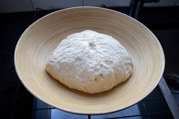 Looking down from above at an elevated view of a ball of raw organic yeast dough in a wide wooden bowl.