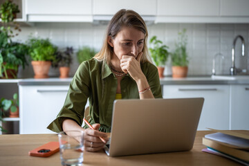 Concentrated female working freelance at home using computer, internet network. Thoughtful woman...