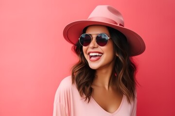 Portrait of a beautiful smiling woman in hat and sunglasses over pink background