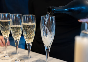 Birthday party, pouring of brut champagne bubbles cava or prosecco wine in tulip glasses with kitchen on background