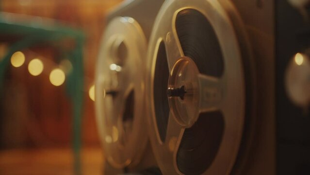 Vintage reel-to-reel tape recorder playing music in room with cozy warm light. Close-up view, rack focus