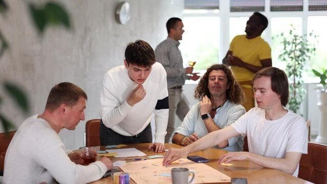 Emotional cheerful young guy playing interesting board game with male friends of different nationalities during bachelor party