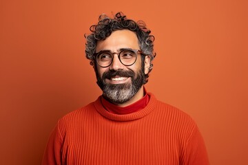 Portrait of a smiling Indian man in red sweater and glasses on orange background