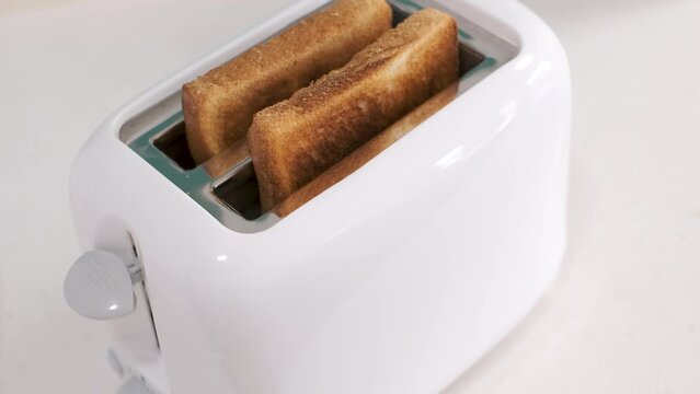Burnt pieces of bread popping out of toaster on a white background, side view.