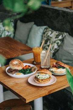 Three pates of burger bagel and sandwich with egg, spinach, cheese and two drink glass on wooden table