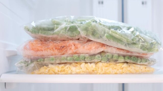 Female hand holds plastic bag with frozen green beans on the background of freezer.