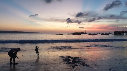 Fototapeta na wymiar Family at sunset by the tropical ocean overlooking fishing boats