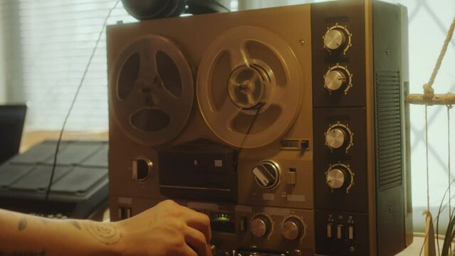 Hand of man turning on vintage reel-to-reel audio tape recorder at home music studio with audio equipment