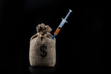 Money bag with US dollar symbol and syringe with liquid on black background
