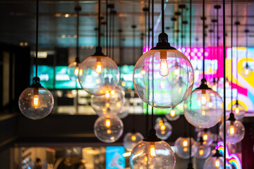 Classic sphere lighting bulbs are glowing in orange warming shade, there are hanging from ceiling in dark environment. Interior cozy style decoration. Close-up and selective focus.