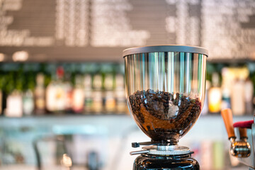 Close-up at stack of fresh coffee bean which is prepared in the coffee grinder machine with blurred background of cafe counter bar. 