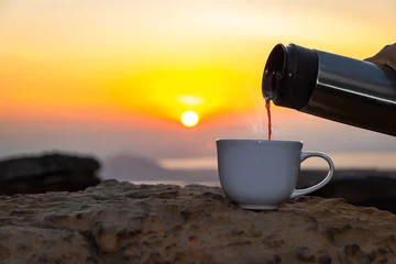 Deurstickers A white cup of hot espresso coffee mugs on the rocks and nature view of the sun background in the morning with sunlight © saelim