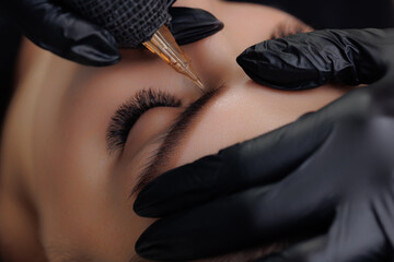 Closeup procedure permanent makeup tattoo for eyebrows of beautiful woman with black brows in...