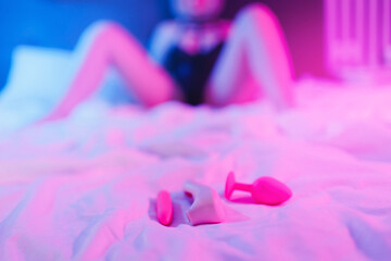Woman in bed holding vibrator clitor and looking at laptop. Adult girl using sex toy, neon color...