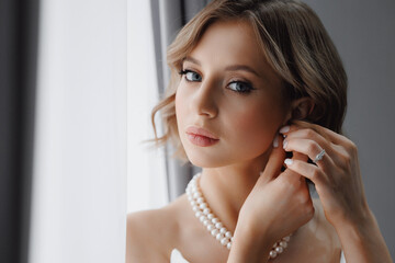 Portrait of happy elegant young woman with white earrings in modern bridal look with classic...