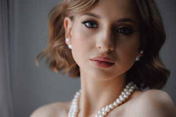 Portrait of happy elegant young woman in modern bridal look with classic hairstyle and makeup with pearl necklace