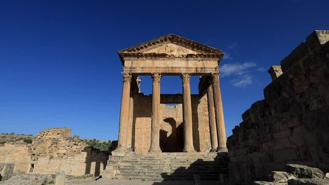 Morning light casts on the Roman ruins of Dougga against a clear blue sky, showcasing ancient architecture