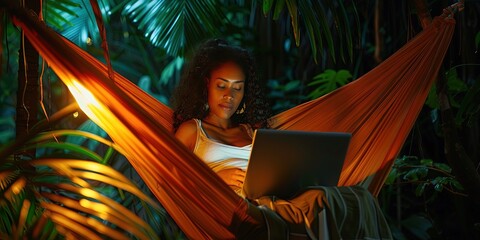 African American woman working remotely using a connected device and cloud-based SaaS software platforms while lounging in a hammock