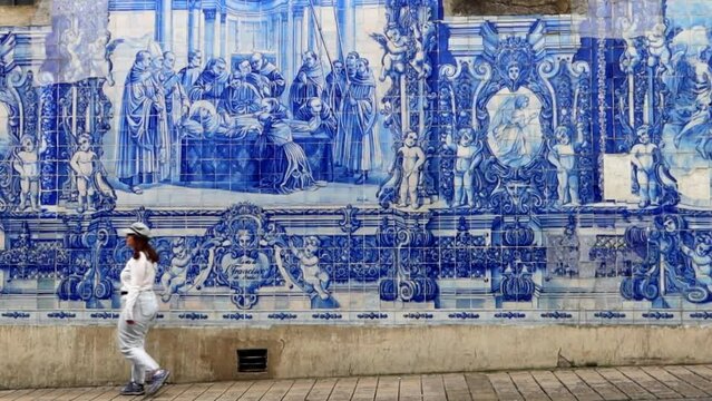 Woman walking in front of the tiled wall of Chapel of the Souls, Porto