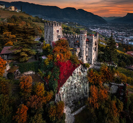 Merano, Italy - Aerial panoramic view of the famous Castle Brunnenburg (Castel Tirolo) with the city of Merano, the Italian Dolomites and colorful sunset sky at background at autumn time - obrazy, fototapety, plakaty