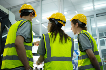 Back view of group young factory worker wearing a hard hat looking at a computer screen used to control production.