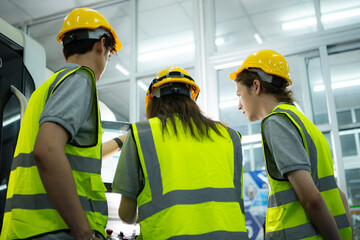 Back view of group young factory worker wearing a hard hat looking at a computer screen used to...