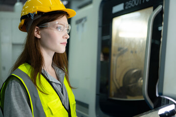 Portrait of a female factory worker wearing a hard hat looking at a computer screen used to control production.