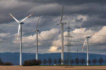 Windräder einer Windkraftanlage in verdichteter Teleaufnahme mit Bergen am Horizont und geschlossener, grauer Wolkendecke