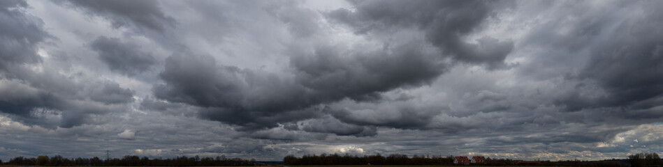 Panoramafoto einer geschlossenen, grauen Wolkendecke mit Gewitter- und Haufenwolken in Unteransicht