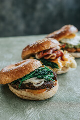 Three breakfast sandwiches stacked toasted bagels with sesame seeds and filled with eggs, spinach, and cheese