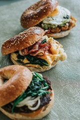 Top-down view of three breakfast sandwiches stacked toasted bagels with sesame seeds and filled with eggs, spinach, and cheese