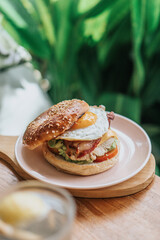 A halved bagel breakfast sandwich with scrambled eggs, bacon, on a pink plate and plant