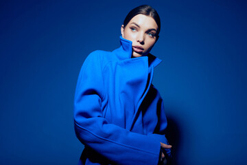 fashion portrait of young elegant woman in blue coat on blue background