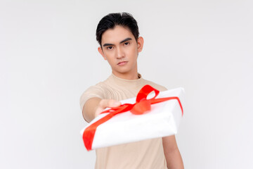 A handsome Asian man seems hesitant while giving a gift wrapped with a red ribbon, conveying mixed...