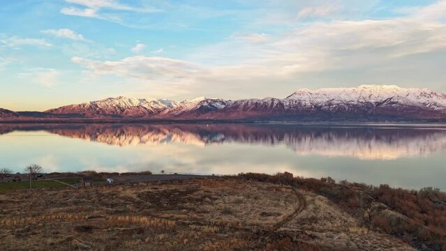 Cinematic time lapse of Utah Lake during calm Winter sunset overlooking sunset reflecting majestic Utah mountains.
