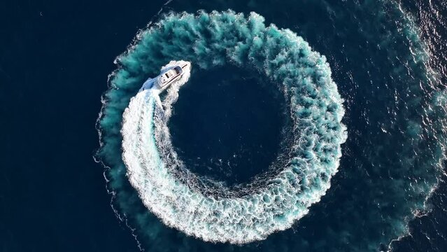 Top down drone shot of luxury yacht driving in a circle at sea while zooming out