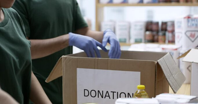 People, hands and box of food for donation, charity or contribution of non profit service. Closeup of man and woman, volunteering workers or team packing groceries, meal or giving back to community
