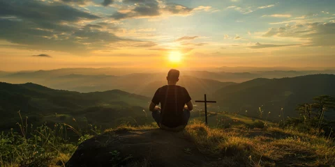 Tuinposter Silhouette of a man sitting on high hill with cross during sunrise or sunset. Regretting sins, missing people who passed away, deeply religious person, praying, thinking about soul and meaning of life © Valeriia