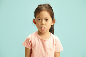 Mischievous Girl Making a Face, Sticking Out Her Tongue Showing to Camera, Studio Portrait Over Blue Isolated